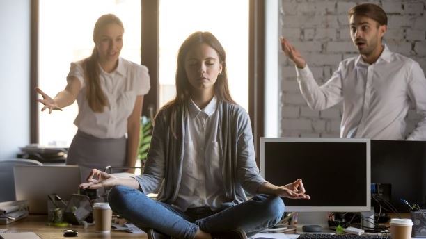 Calm serene employee meditating in office ignoring not listening to panicking colleagues