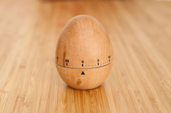 Wooden egg-shaped kitchen timer set to zero, placed on a bamboo surface.