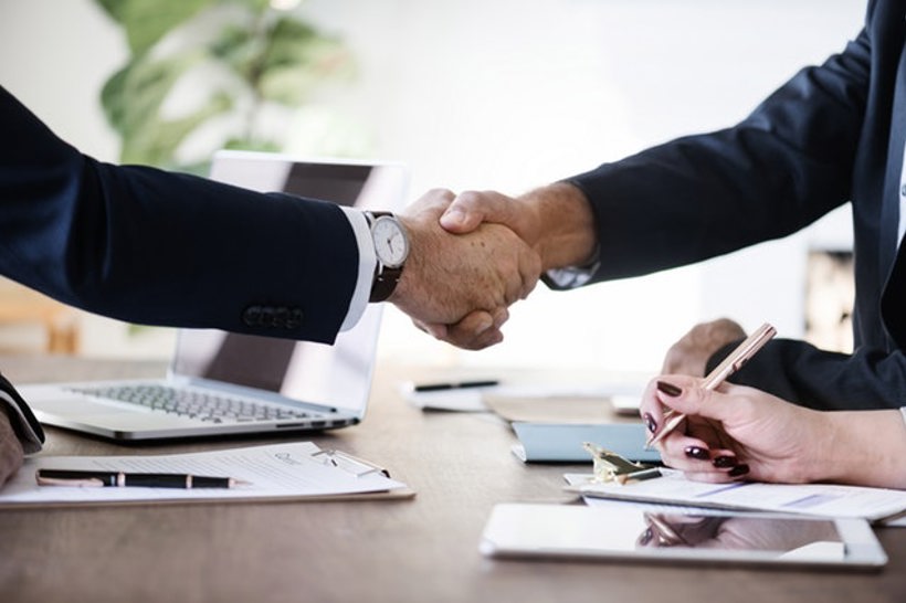 Two people shaking hands over desk with laptop and documents