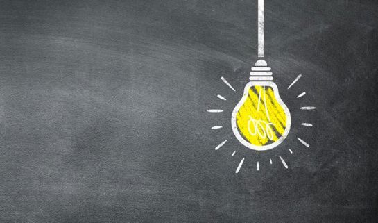 Chalk drawing of a glowing yellow light bulb on a blackboard, symbolising ideas or innovation.