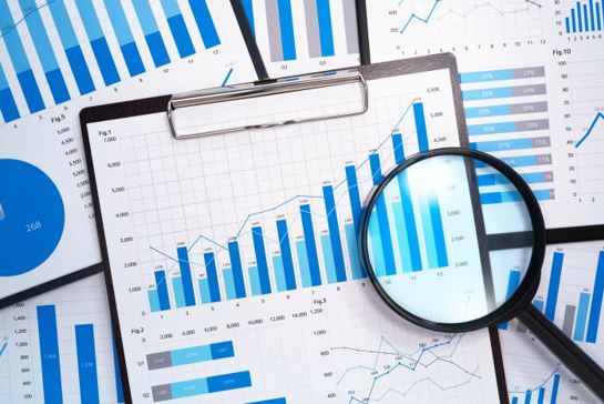 Magnifying glass and charts showing growth on clipboard